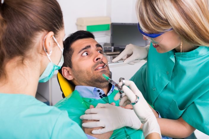 Female dentist with assistant and scared male patient at dental clinic